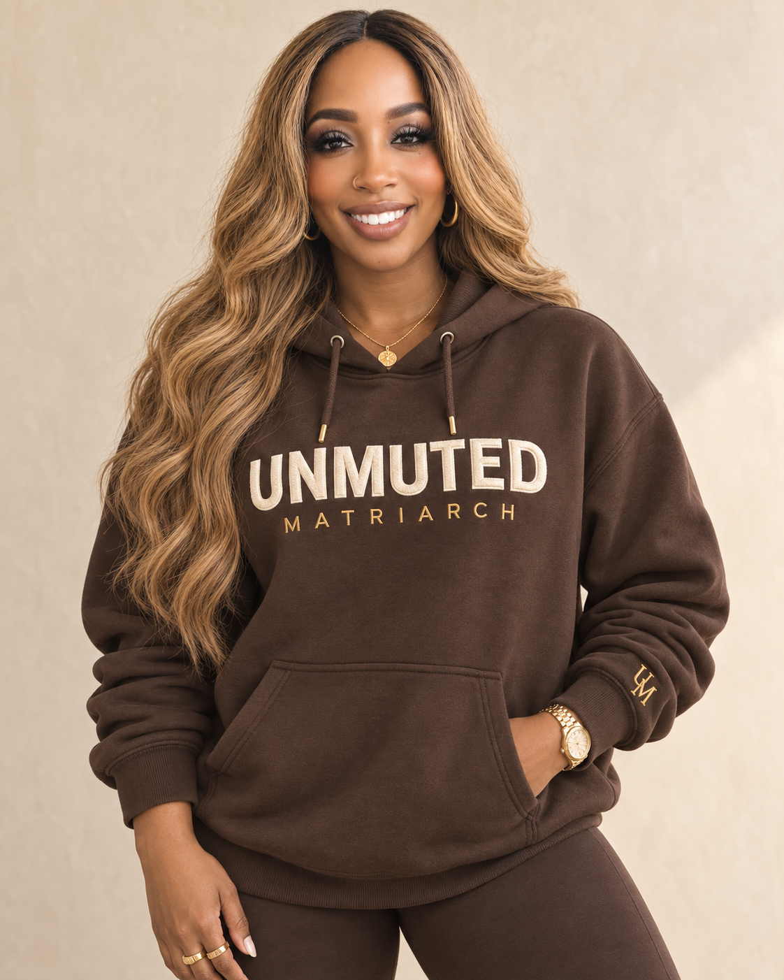 Woman wearing a chocolate Unmuted Matriarch hoodie with gold lettering